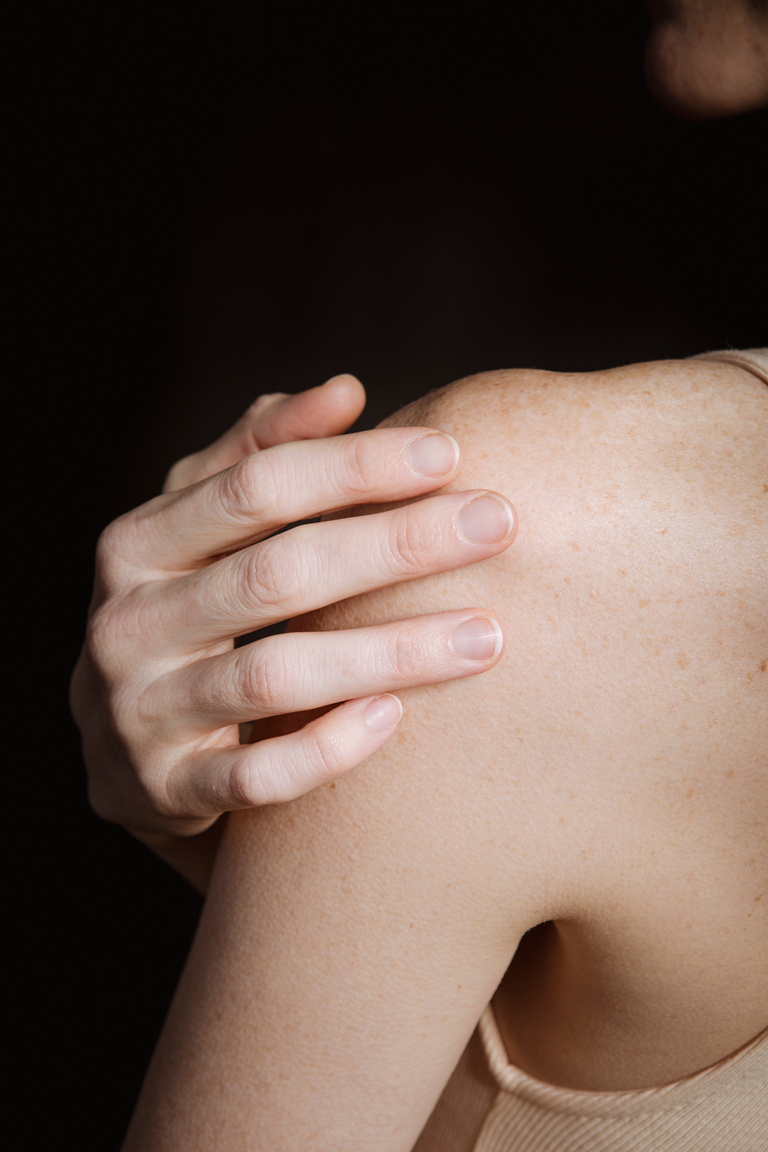 Slim female touching shoulder against dark background